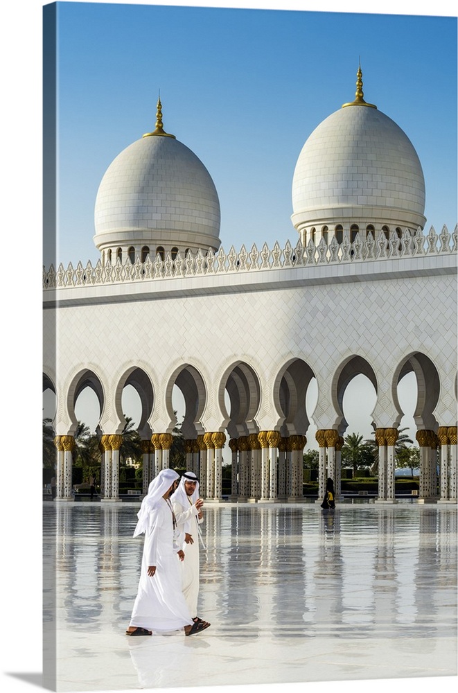 Two Middle Eastern men traditionally dressed walking in the courtyard of the Sheikh Zayed Mosque, Abu Dhabi, United Arab E...