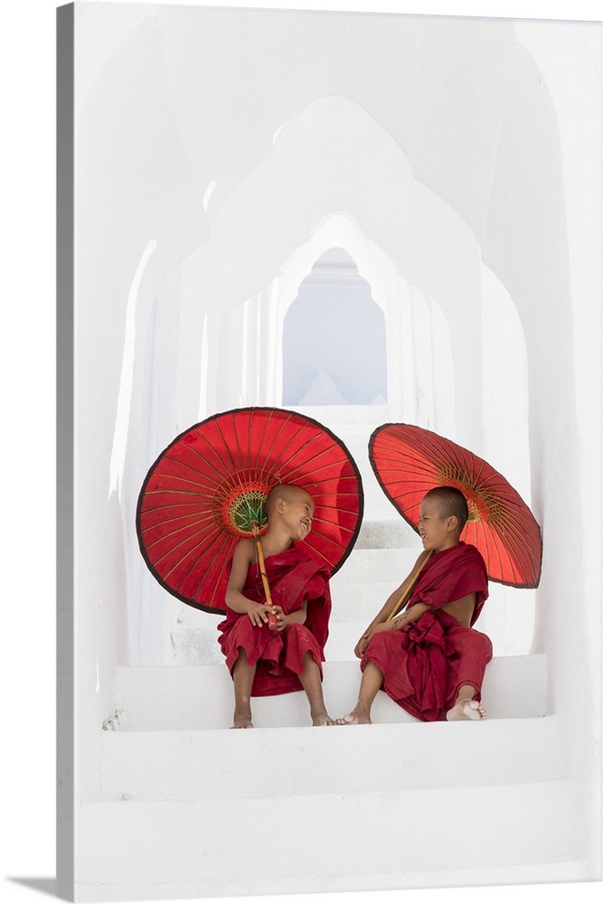Two young Buddhist monks holding red umbrellas have fun in Hsinbyume Pagoda, Mingun, Mandalay, Myanmar.