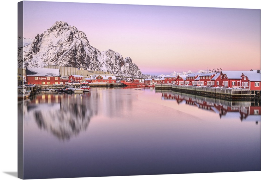 Pink sunset over the typical red houses reflected in the sea. Svollvaer Lofoten Islands Norway Europe.