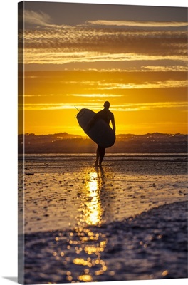 UK, Cornwall, Polzeath, A woman comes in from an evening surf against a stunning sunset