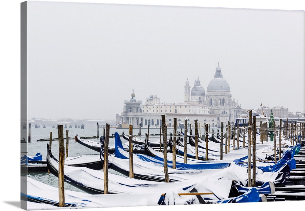 Winter snowfall in the city of Venice, gondolas covered by snow and in the background the church of Santa Maria della Salu...