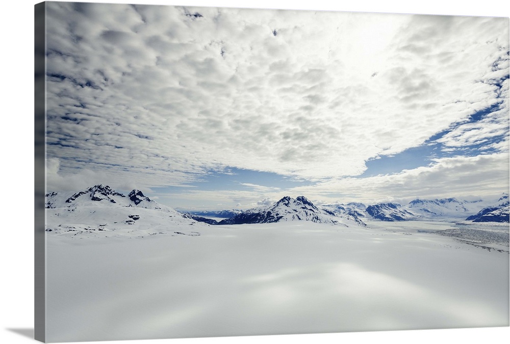 A landscape covered in snow high in the mountains of Alaska, under a cloudy sky.
