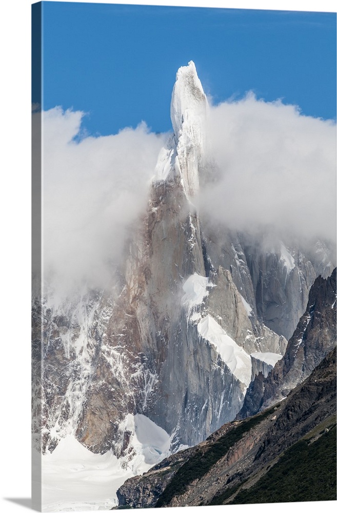 Photograph of snow-covered mountain spires in South America surrounded thick fluffy clouds.