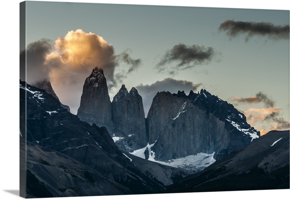 Photograph of mountain spires in South America cast in shadow, with illuminated clouds in the sky.