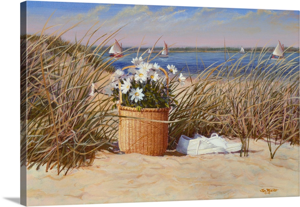 Basket of flowers with white sneakers in the sand and sea grass with sailboats in the water.