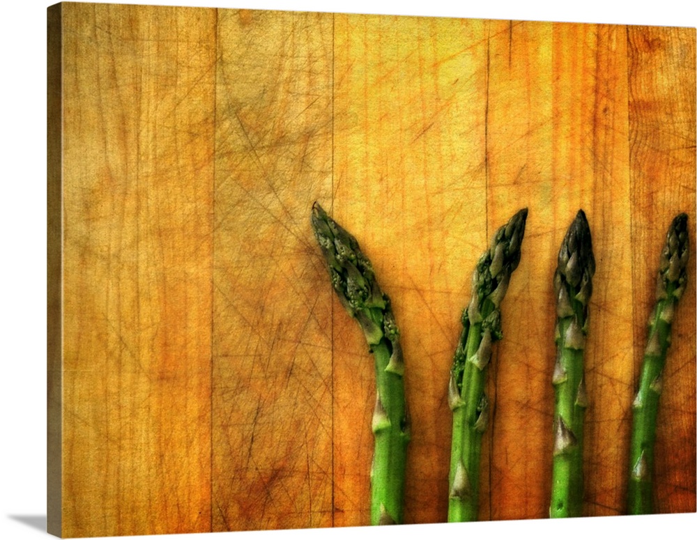 Four green asparagus spears laying on a wooden surface.