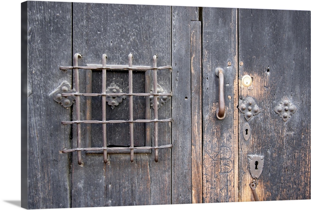 Oversized, horizontal close up photograph of an old wooden door with elaborate safe opening and decorative metal fixtures.