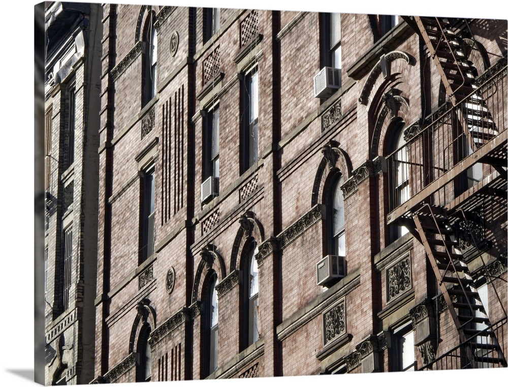 This is a horizontal photograph of the faoade of a brick buildingos window, window mounted AC units, and an iron wrought f...