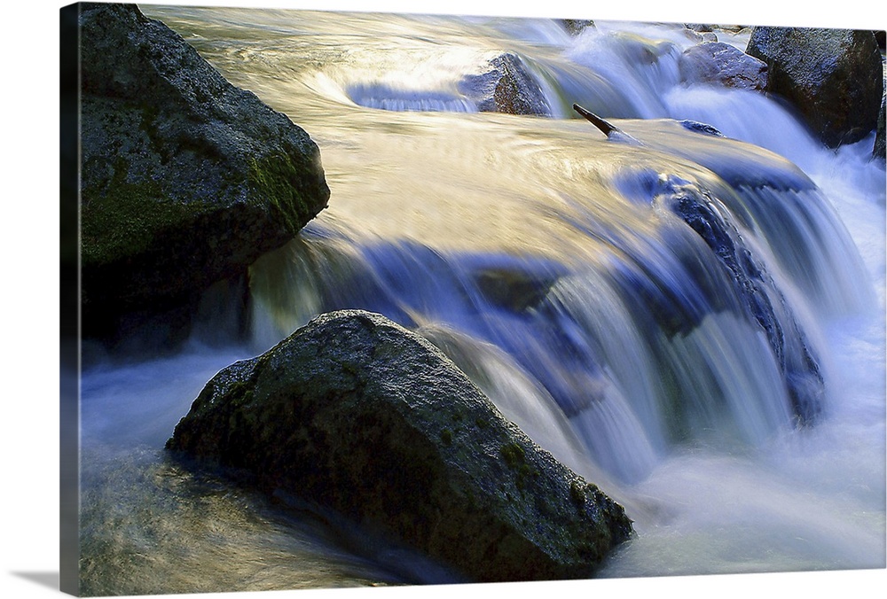 Long exposure shot of water in a stream rushing over a rocky riverbed, creating a small waterfall.