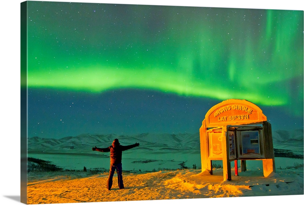 A man looks in awe at the northern lights near the Arctic Circle sign.