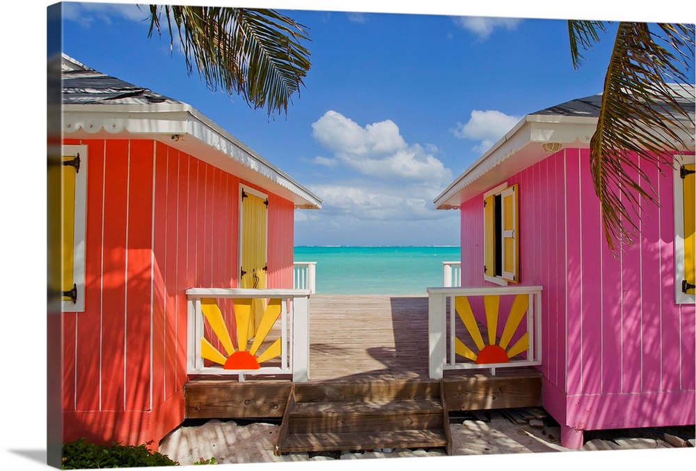 Two colorful cabanas sit on the beach and have a small walking path in between that leads down to the water.