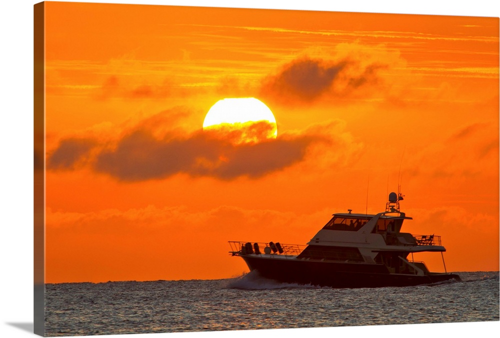 Boat passing in front of a big glowing sun during a spectacular sunset over the Atlantic Ocean.