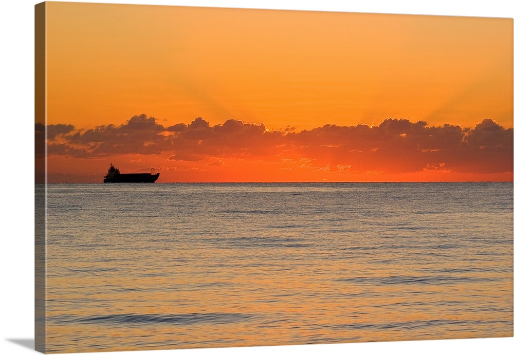 A silhouetted ship moments before the sun rises over the horizon.