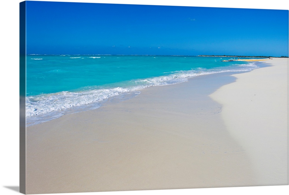 A beautiful picture of teal colored ocean water coming up onto the white sand beach. A clear blue sky hangs over.