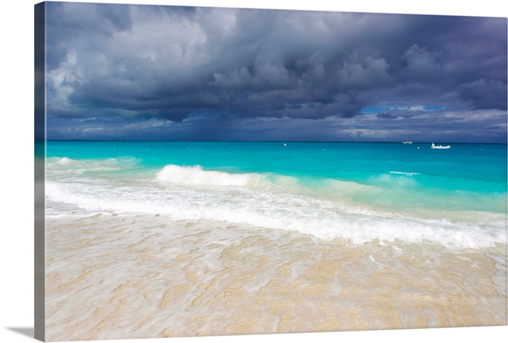 Storm clouds roll in over turquoise waters and a beach.