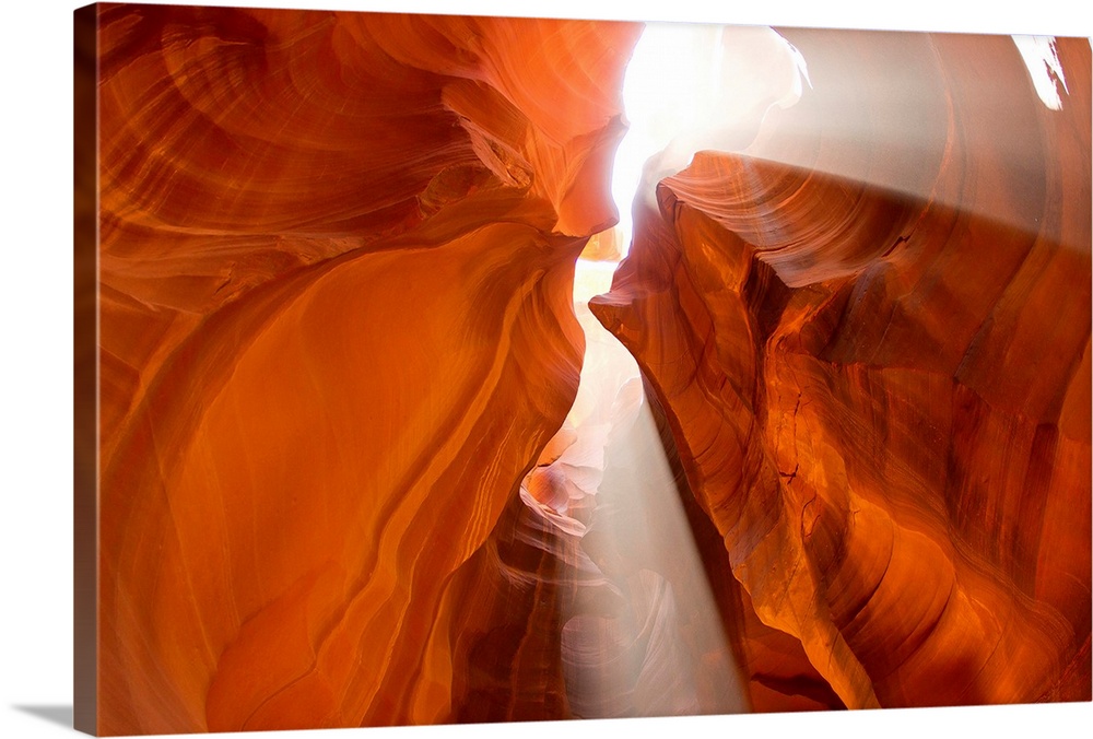 Rays of sunshine come through the cracks of a canyon as the photograph is taken looking up at them.