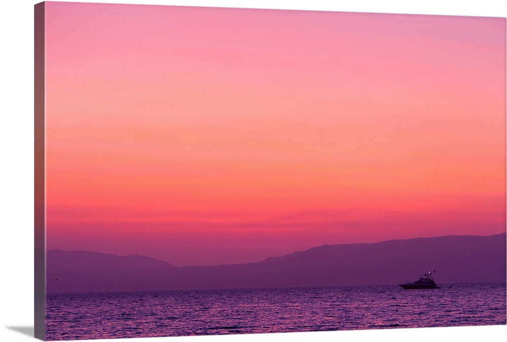 Sunset turns the sky pink and purple as a lone boat floats offshore.