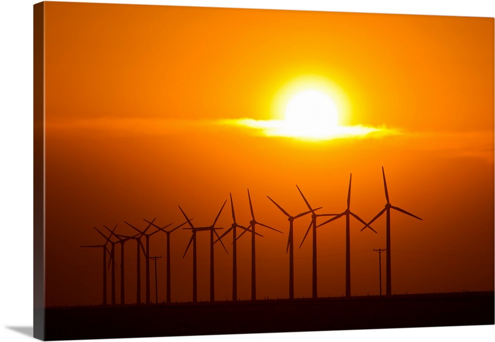 The sun sets behind a row of spinning windmills or wind turbines.