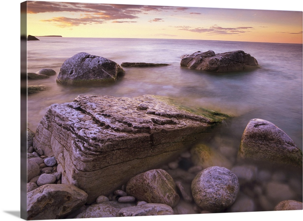 Photograph of rocky shoreline filled with large boulders under a cloudy sky.