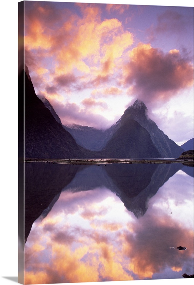 Big, vertical photograph of Mitre Peak, reflecting in the still water of Milford Sound, as the sun sets in a vibrant, colo...