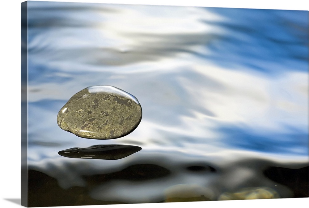 A rock just about to hit the water's surface. The surface tension of the liquid keeps the pebble encased as it hovers over...