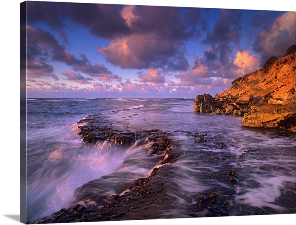 Large photograph displays the powerful waves of the Pacific Ocean crashing into the rocky shores of an island.