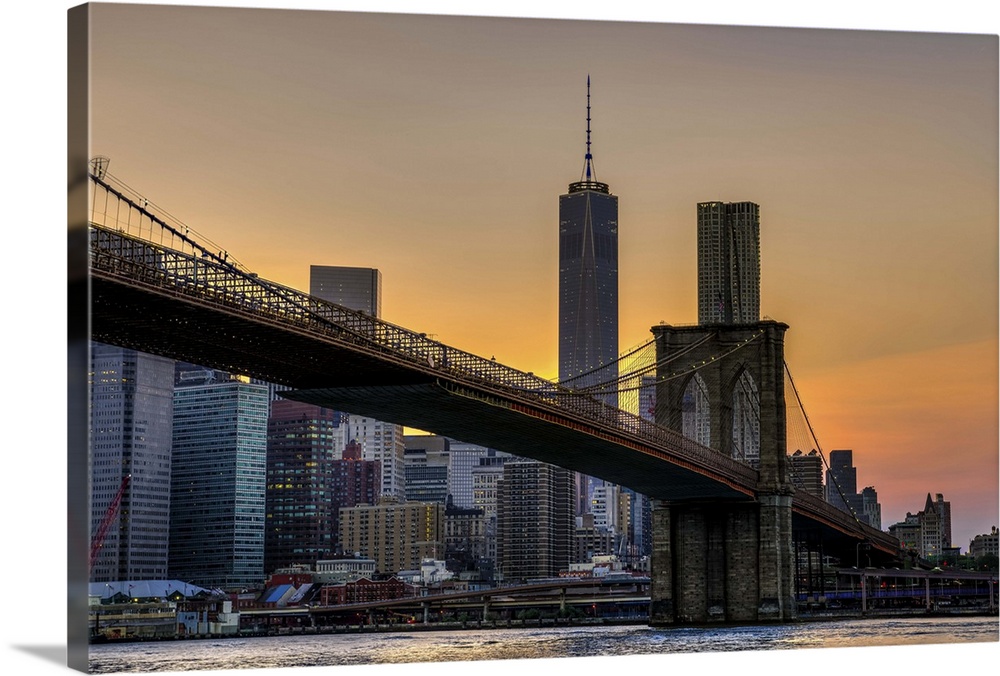 A photograph of the Brooklyn bridge at twilight with One World Trade standing tall in the background.
