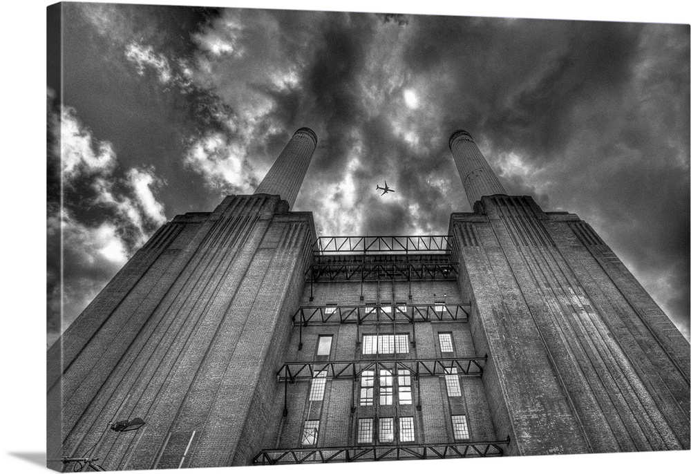 A black and white photograph looking up at a power station with dramatic clouds above.