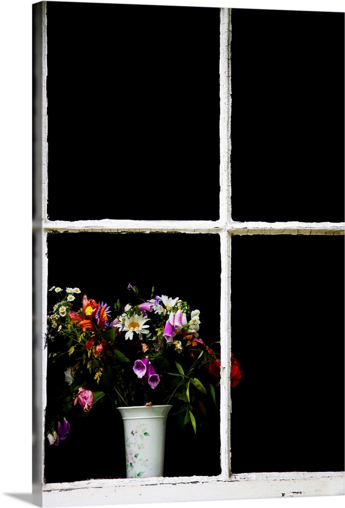An old white window frame with a white vase filled with a jumble of cottage garden flowers.