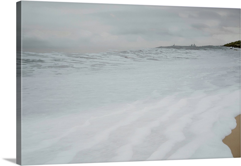Photograph of foamy sea water rushing up the sandy shore on a cold Winter's day.