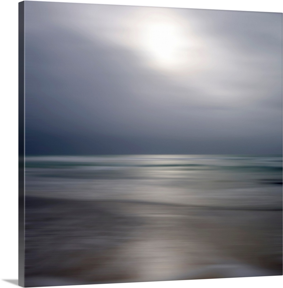 Giant photograph displays an ocean gently making its way to a sandy shore while underneath a cloud-filled sky.