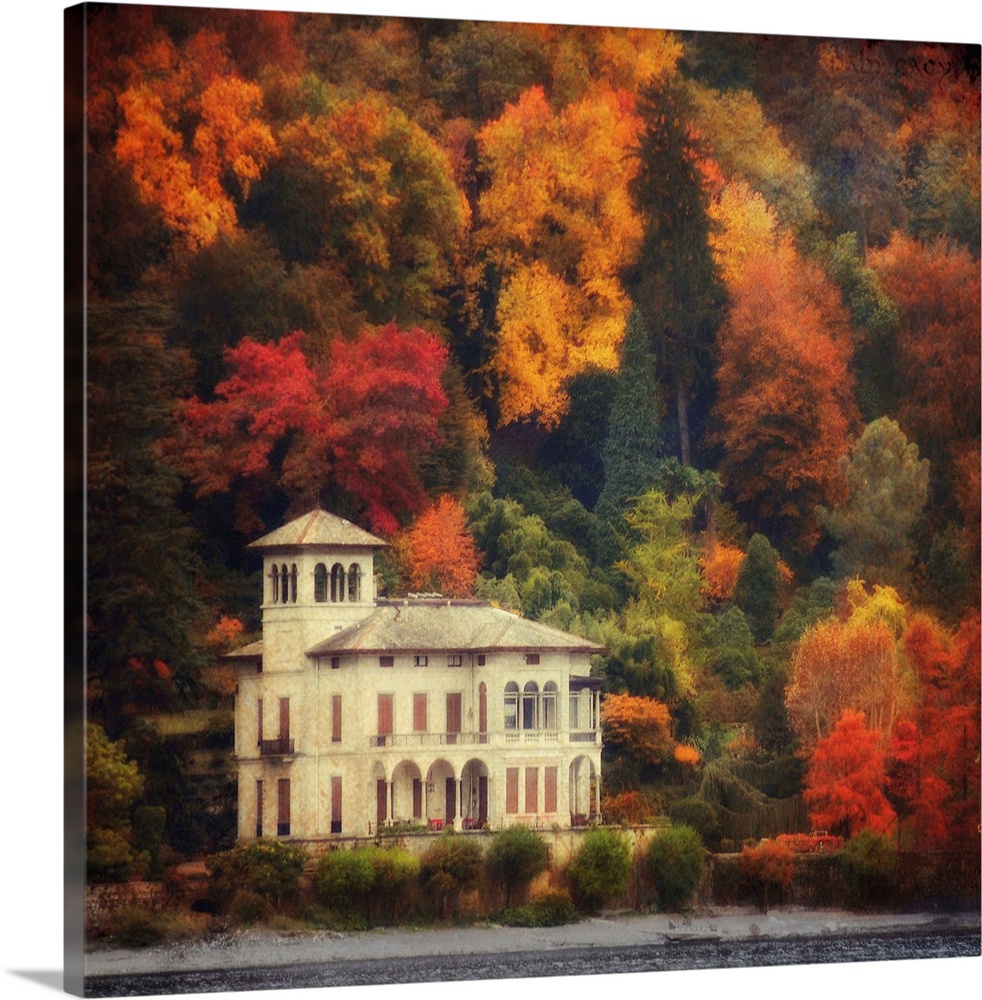 This is a landscape photograph on square shaped wall docor that shows a lake side villa surrounded by a forest of fall fol...