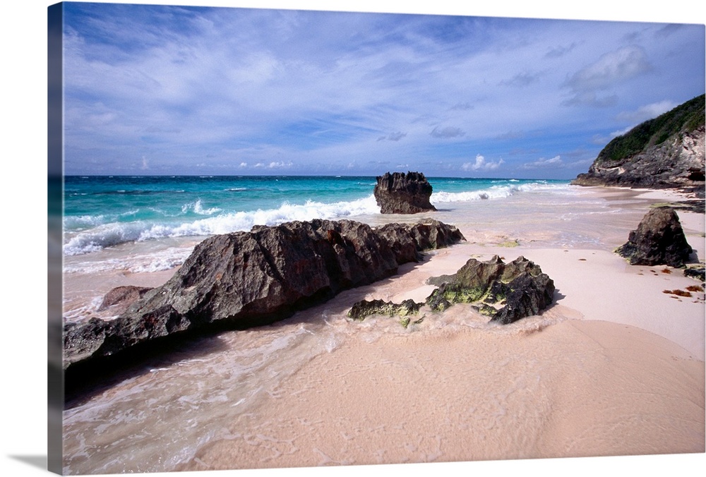 View of a Pink Sand Shore, Elbow Beach, Bermuda, large rocks half-buried in the sand and foamy waves coming in from the oc...