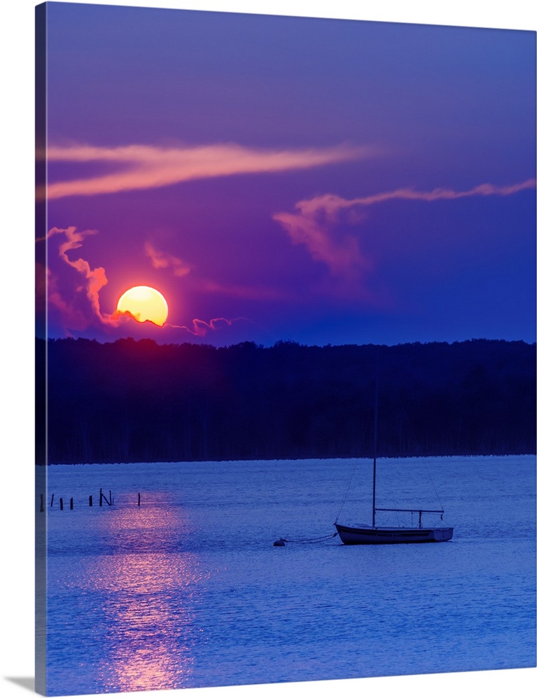 The setting sun glowing vividly against the violet evening sky, over a lone boat on the water, at twilight.