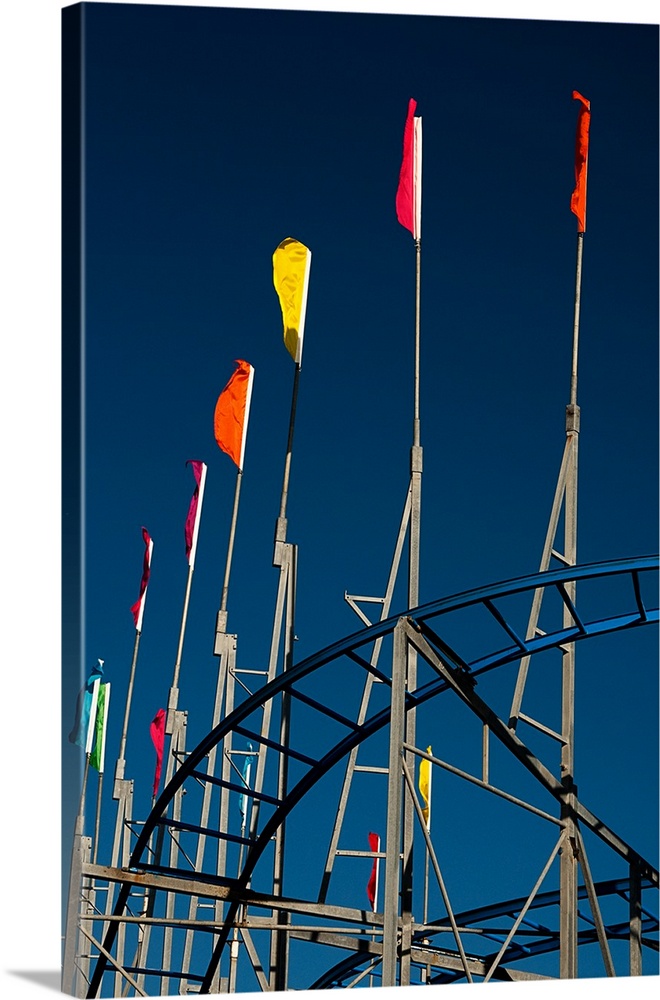 Colorful flags flying over the side of a roller coaster on a boardwalk.