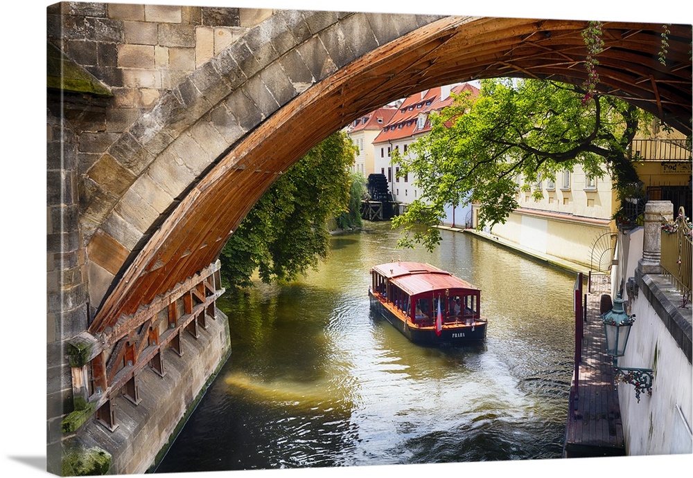 A boat on the water passing under an arched bridge in Prague, Czech Republic.
