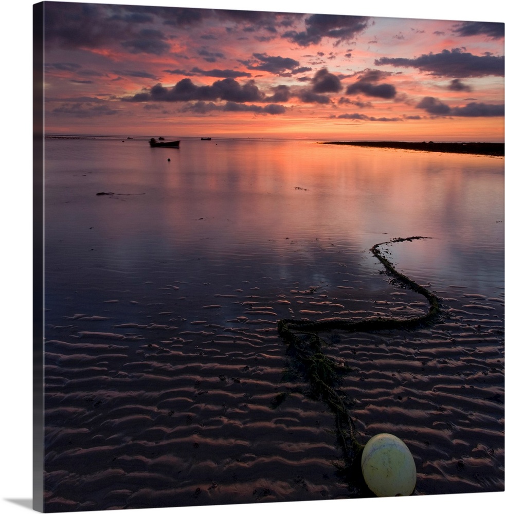 A dramatic warm golden peach glowing sunrise over wet sand patterns with a bouy and chain and reflecting water.