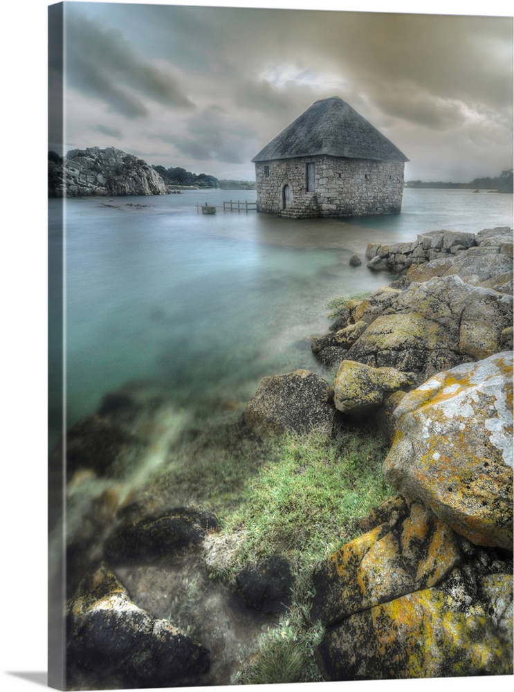 Old mill house called Moulin du Birlot, on Brehat Island in Brittany, in France at high tide, vertical view with rocks at ...