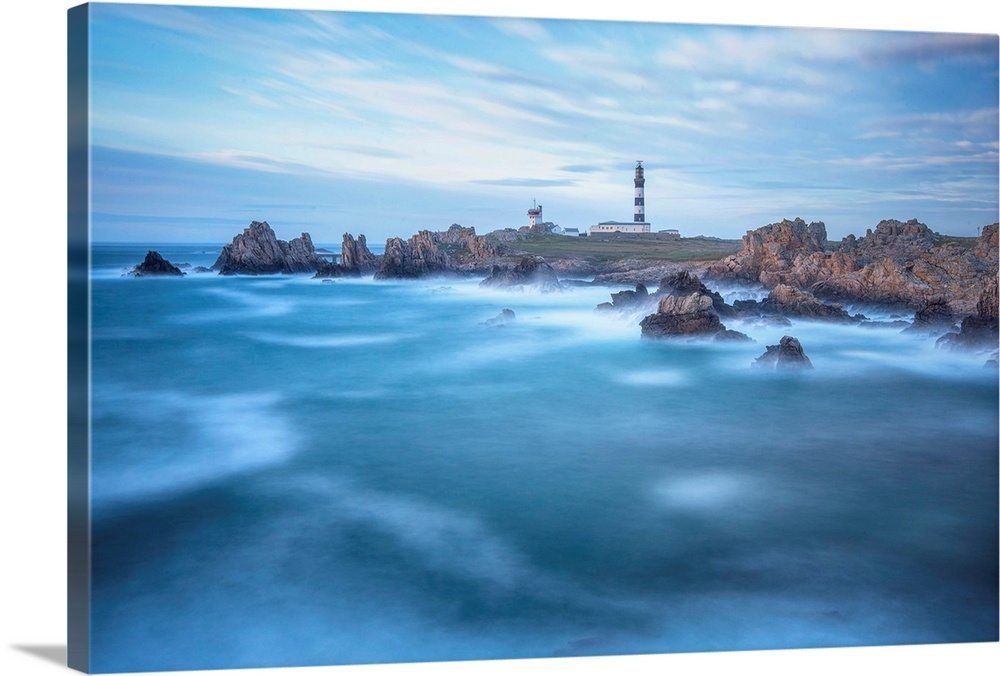 Fine art photo of a lighthouse on a rocky coast with a cloudy sky and deep blue ocean.