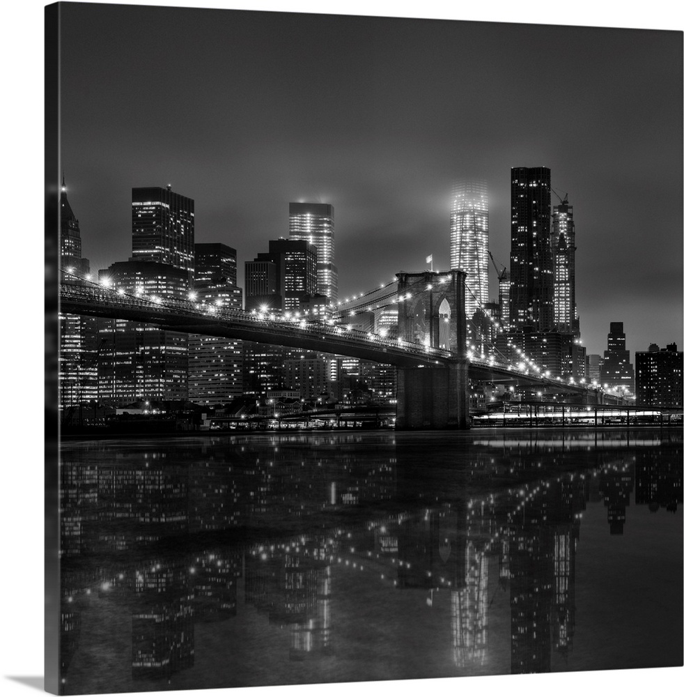 Black and white photograph of New York city's skyline at night with the Brooklyn bridge in the foreground.