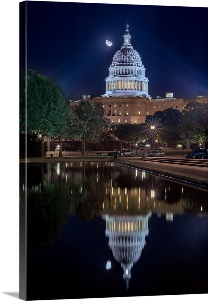The United States capitol building mirrored in the water below at night.