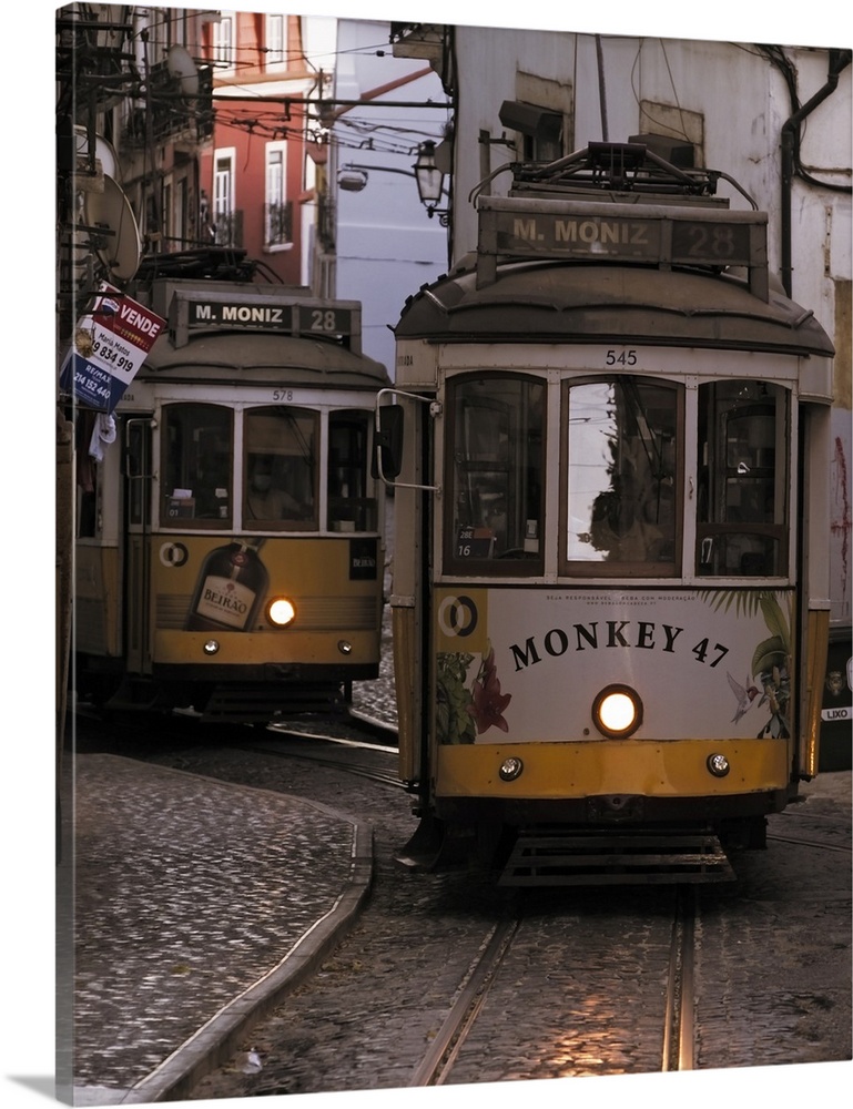 Vintage trams of line 28 traveling in a narrow street in Alfama district of Lisbon at dusk, Portugal, Europe.