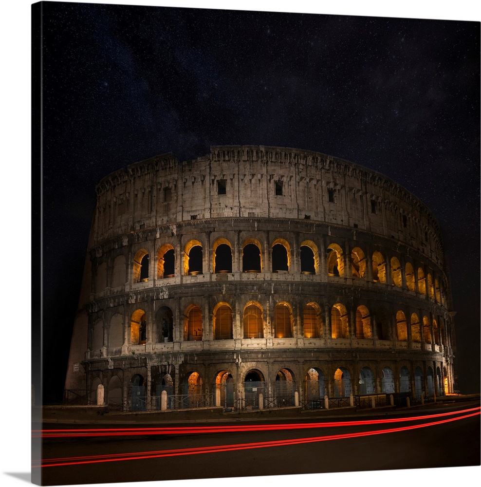The Colosseum in Rome illuminated at night with light trails from passing cars.