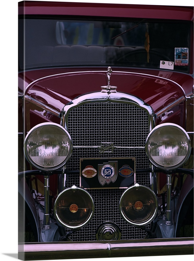 The front grille and round headlights of a maroon colored vintage car.