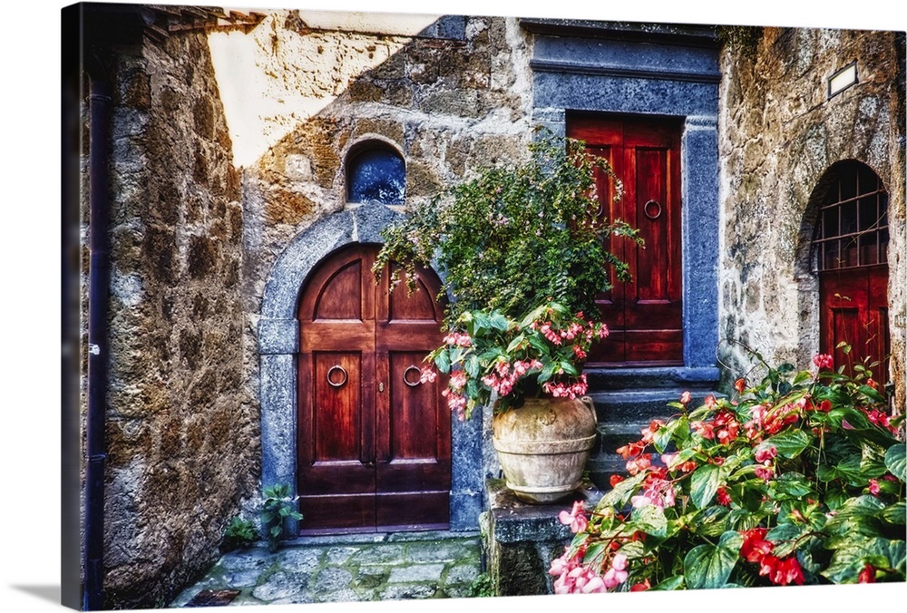 Two wooden doors in a stone wall surrounded by blooming potted flowers.