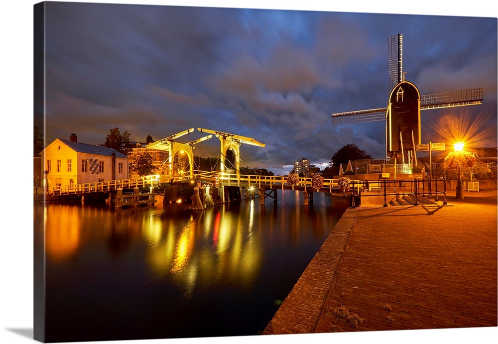 View of a canal with a small bridge and windmill at night, Leiden, South Holland, Netherlands.