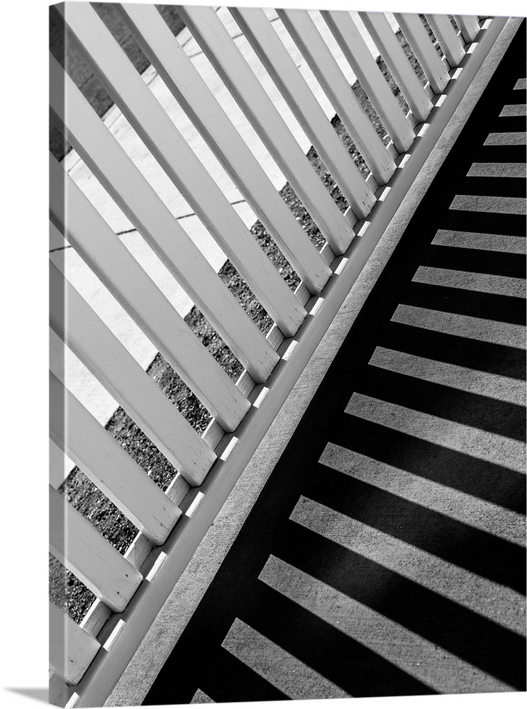 Monotone image of a fence casting long striped shadows on a walkway.