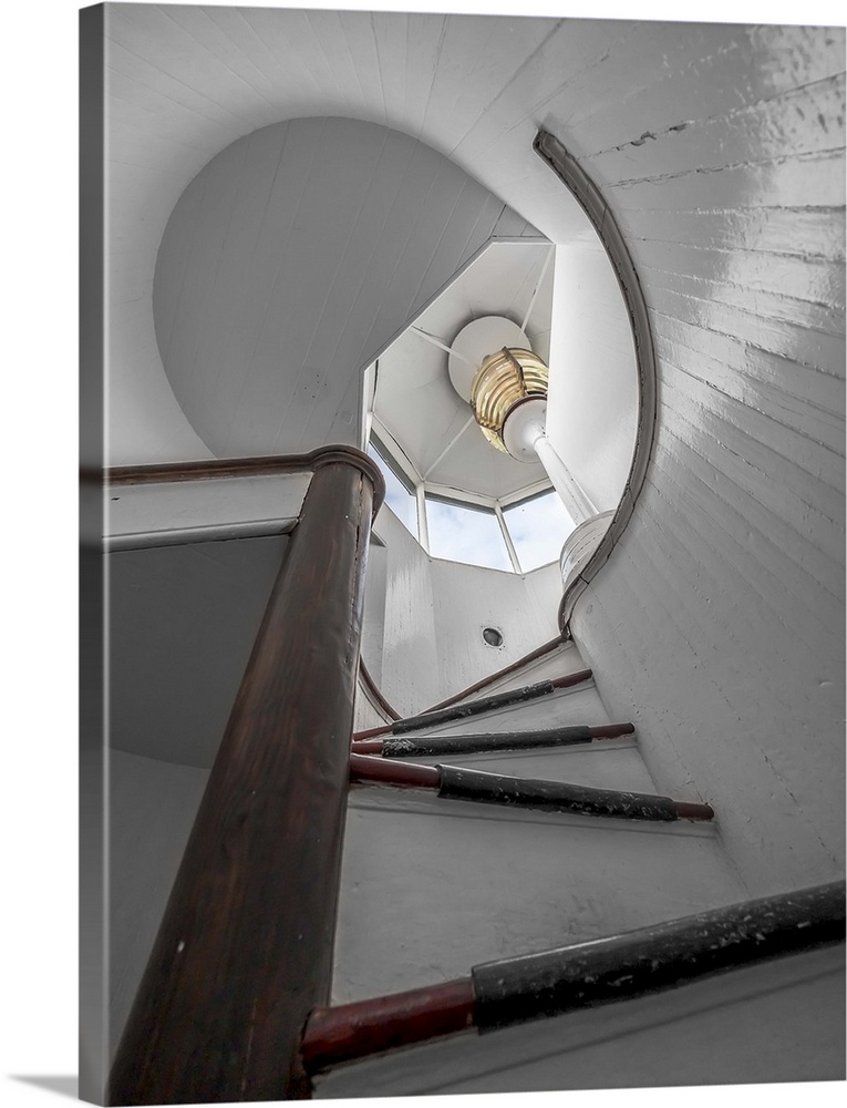 View up the stairs of a lighthouse with a view of the lamp upstairs.