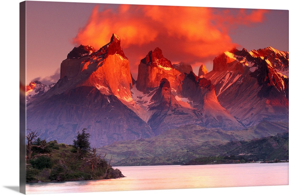 This breathtaking view is of immense mountains that have warm tones at the very top from the sunset sky above.