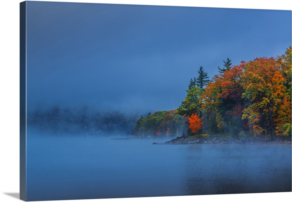 Dense fog over a lake in the evening with autumn trees.